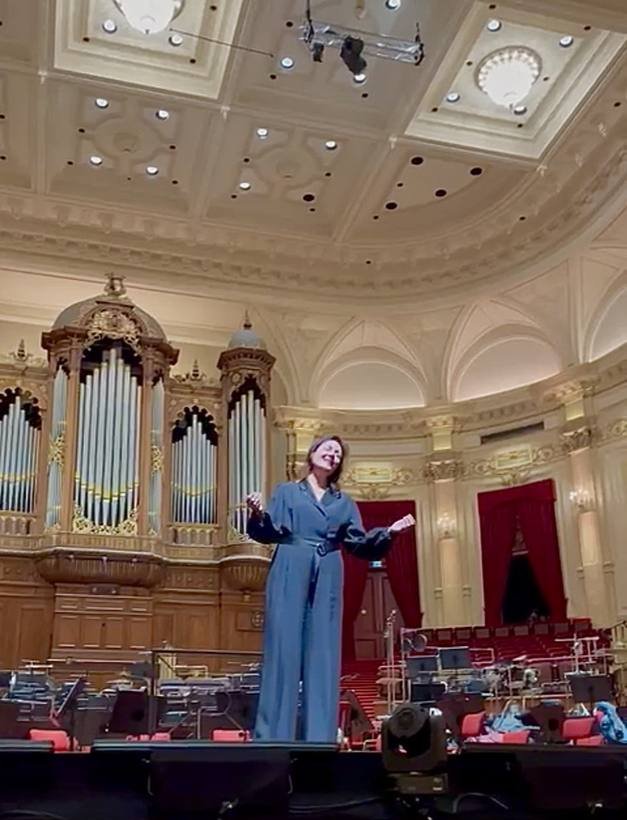 Debby Mureau op het podium van het Concertgebouw. Een spot laat steeds meer zien, eerst Debby, dan iedereen in het Concertgebouw.