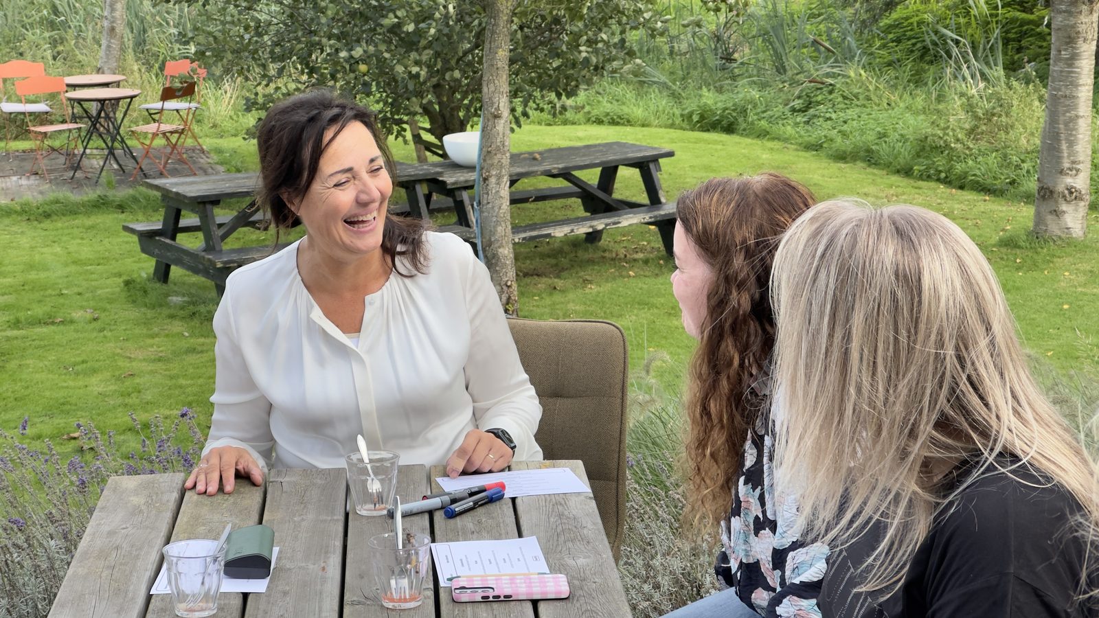 Debby Mureau lacht in een gesprek aan een tuintafel